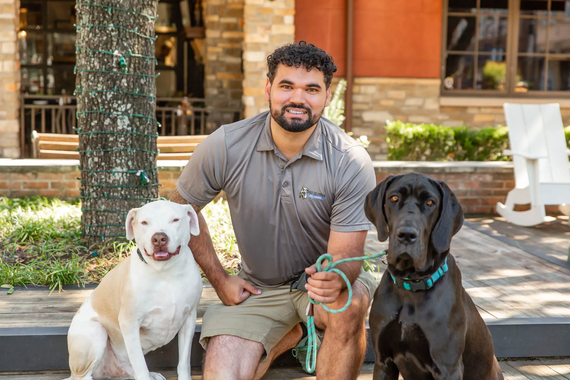 Man posing outdoors with three dogs of different breeds.